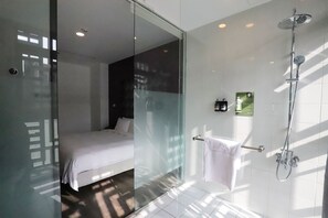 A modern bathroom with a glass shower enclosure, a white bathtub, and a glass door leading to a bedroom with a bed. - Aroma Chew Hotel (Taichung)
