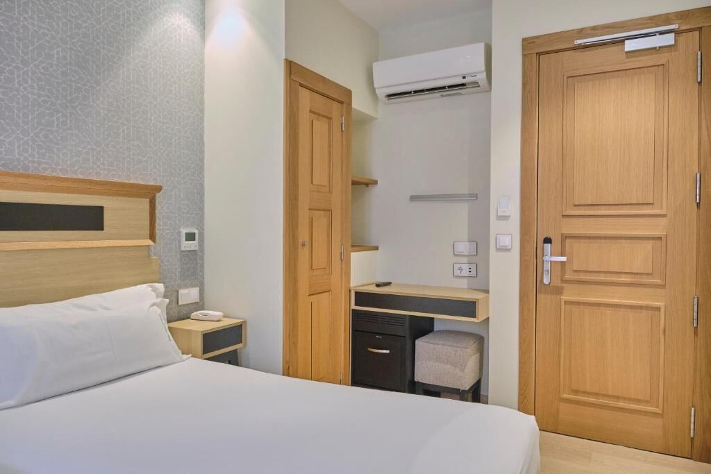 A hotel room with a bed, a desk, a chair, an air conditioning unit, and a wardrobe.