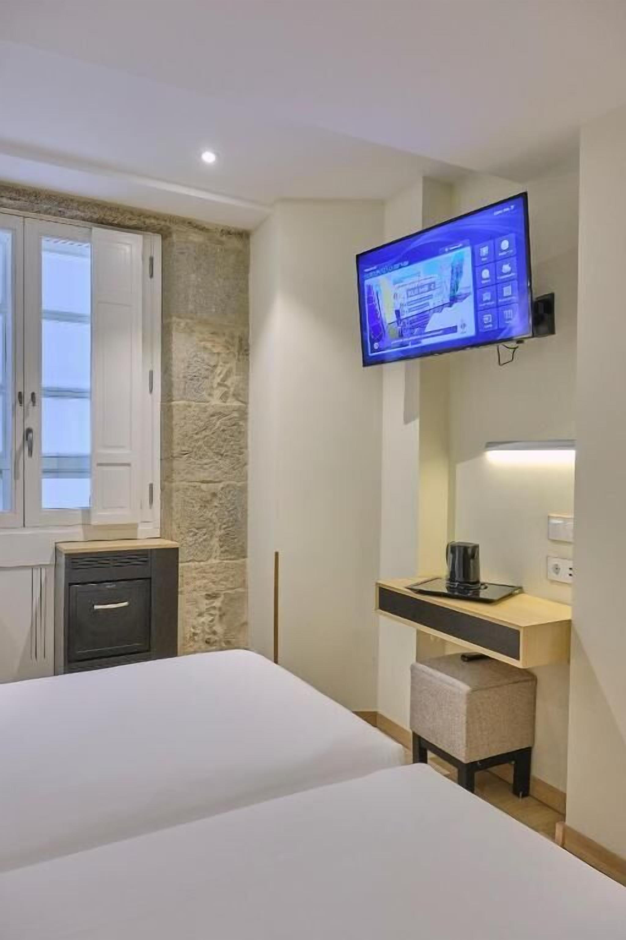 A hotel room with a bed, a desk with a computer, a television mounted on the wall, and a window with a view of the outside.
