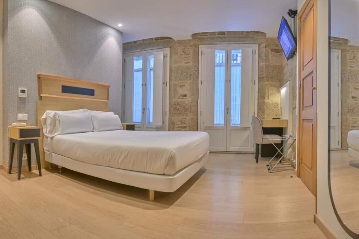 A bedroom with a bed, bedside table, and a TV mounted on the wall.