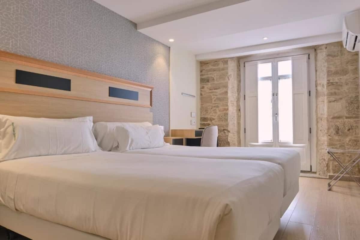 A hotel room with a large bed, a desk, and a stone wall.