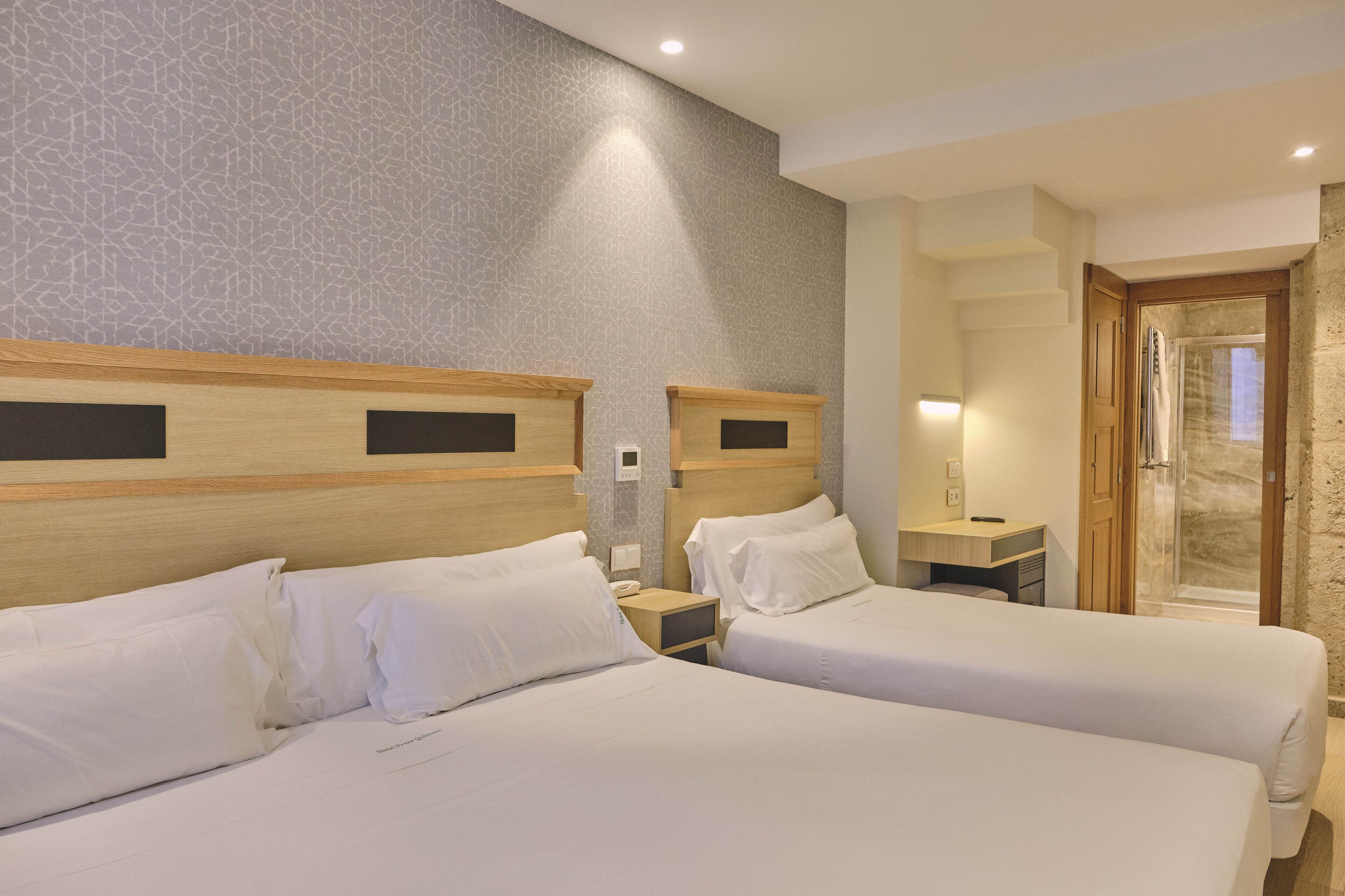 A hotel room with two beds, a wooden headboard, a nightstand, a desk, and a shower area.