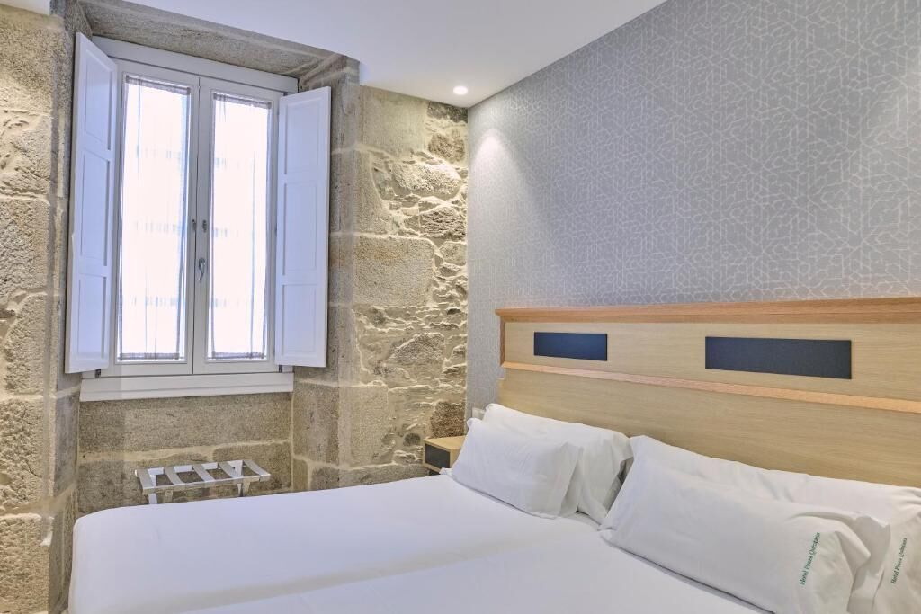 Un dormitorio con pared de piedra, cabecera de madera y ventana con contraventanas.