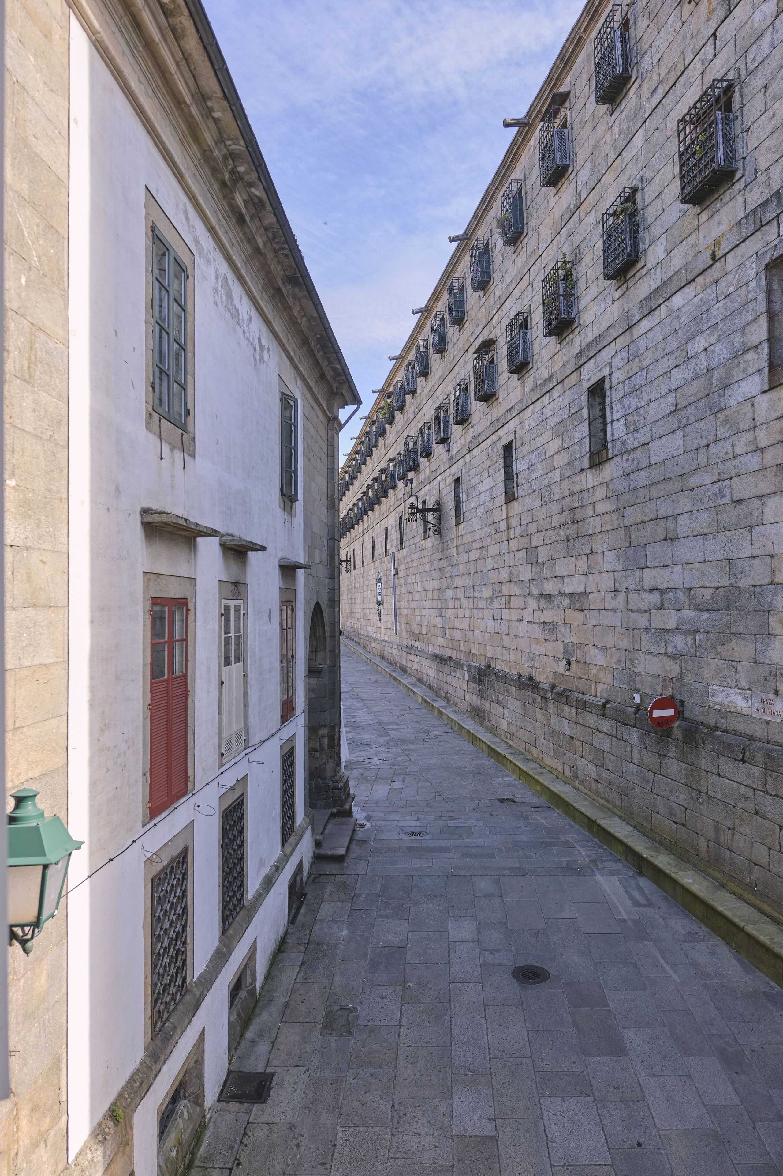 A narrow street flanked by historic buildings with arched doorways and a row of windows with metal grilles.