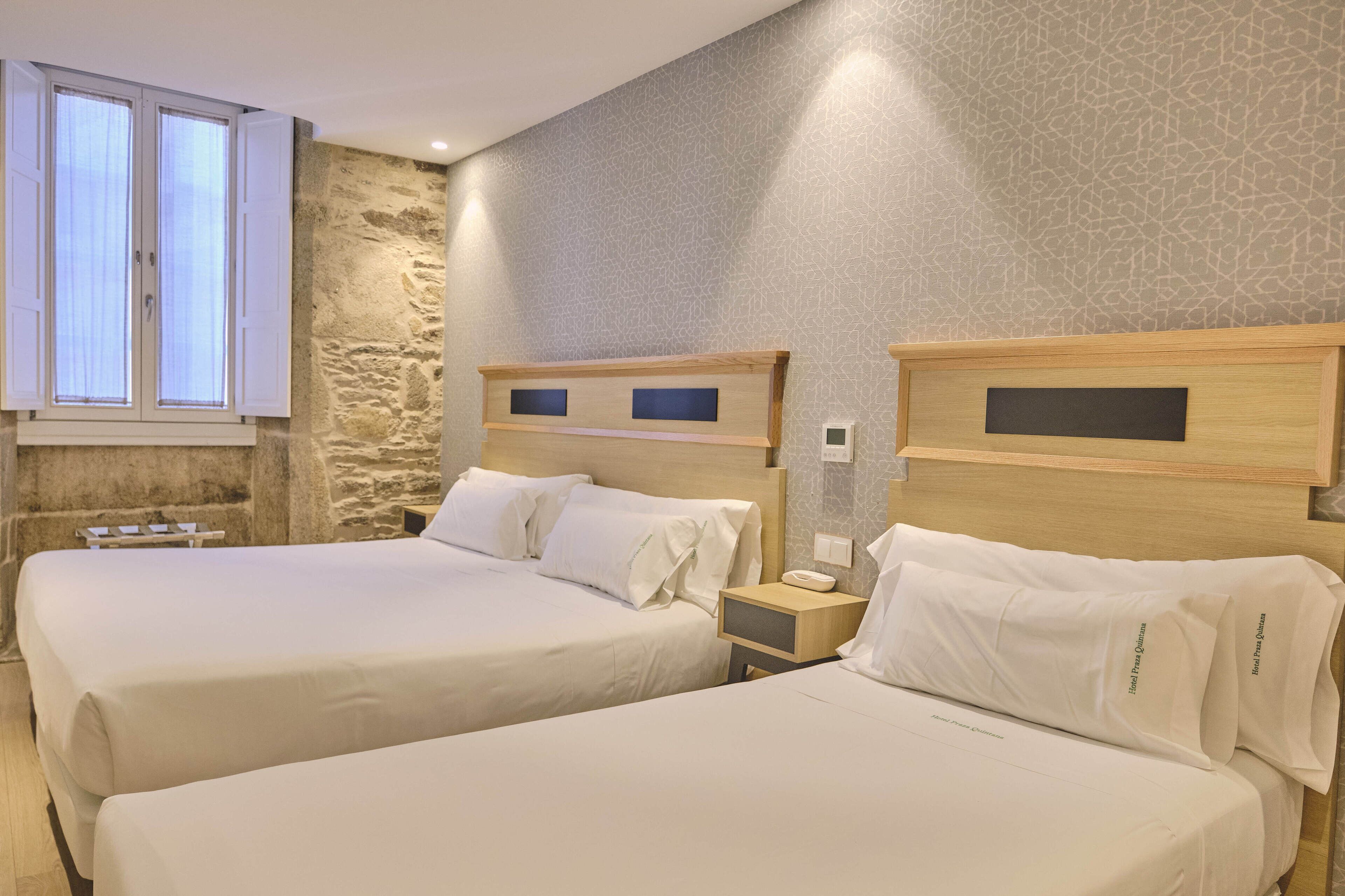 Ein Hotelzimmer mit zwei Betten, einer Wand mit Steinverkleidung und einem Fenster mit Vorhängen.