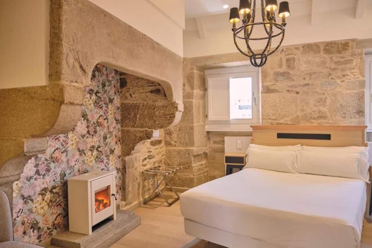 A bedroom with a stone fireplace, a bed, and a chandelier.