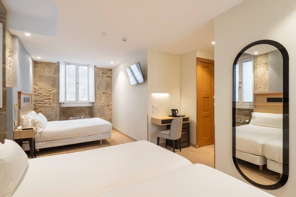 A hotel room with a bed, a desk, a chair, a TV, and a mirror.