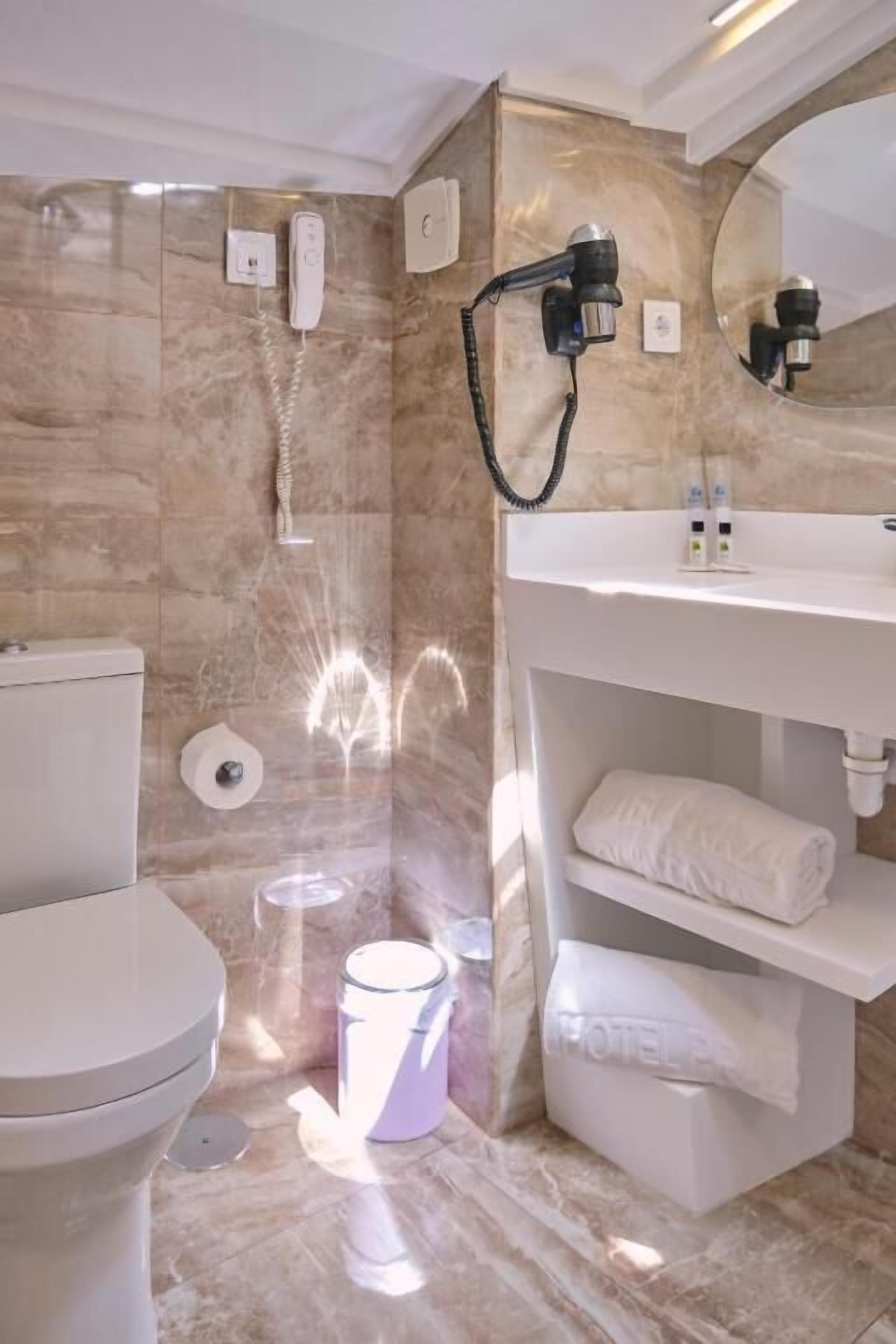 A bathroom with a marble wall, a white sink with a towel rack, and a shower area.