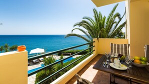 A balcony with a view of the sea, a dining table with plates and glasses, and a small pool area. - Preveli Villas (Agios Vasileios)
