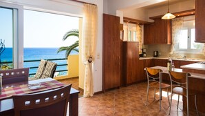 A kitchen with wooden cabinets, a dining area with a table and chairs, and a view of the ocean. - Preveli Villas (Agios Vasileios)