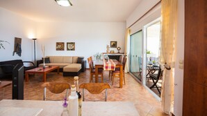 A living room with a sofa, coffee table, and dining table set. There is a TV, a lamp, and a bottle on the table. - Preveli Villas (Agios Vasileios)