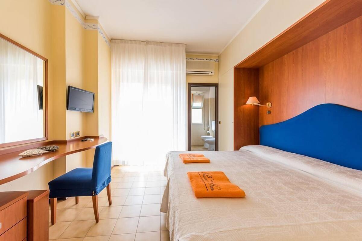 Ein Hotelzimmer mit Bett, Schreibtisch, Stuhl, Fernseher und einem durch eine offene Tür einsehbaren Badezimmer.