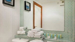 Une salle de bain avec un lavabo, des toilettes et un miroir. Des serviettes sont pliées sur le comptoir et des articles de toilette sont posés sur le lavabo.