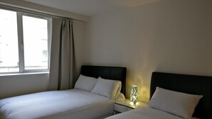 Une chambre d’hôtel avec deux lits, une table de chevet, une lampe et une fenêtre avec des rideaux.