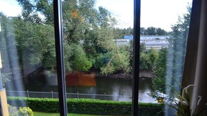 A view through large windows of a river, greenery, and a distant building. - MetroStays - Riverside Apartment (Dublin)