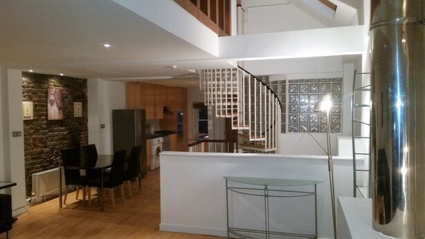 A modern kitchen with wooden cabinets, a dining area with a glass table, and a staircase with a metal railing. - MetroStays - Stephen's Green 7-3 (Dublin)