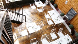 An outdoor dining area with white tables and chairs, a wooden deck, and a staircase. - Casona Recoleta (Santiago)