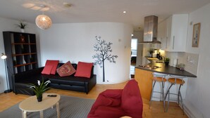 A modern living room with a black sofa, red cushions, a red bean bag, a small round table with a plant, and a wall-mounted tree decoration. - MetroStays - Stephen's Green 7-2 (Dublin)