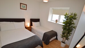A hotel room with two beds, a bedside table with a lamp, a window with a plant, and a framed picture on the wall. - MetroStays - Stephen's Green 7-2 (Dublin)