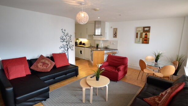 A modern living room with a black sofa, red cushions, a small round table, and a kitchen in the background. - MetroStays - Stephen's Green 7-2 (Dublin)