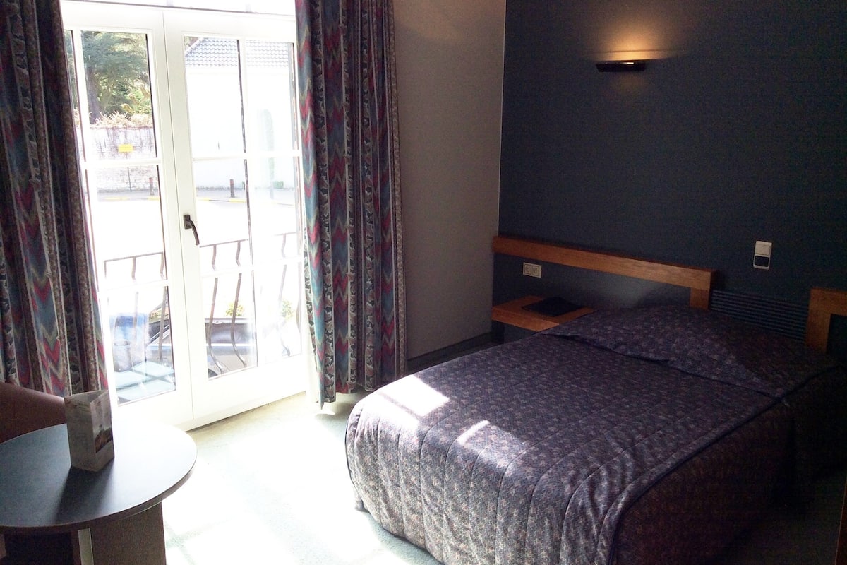A bedroom with a bed, a small table, and a sliding glass door leading to an outdoor area.