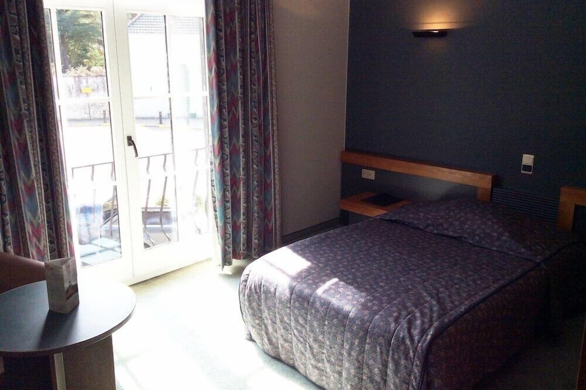A bedroom with a bed, a small table, and a view through a glass door.