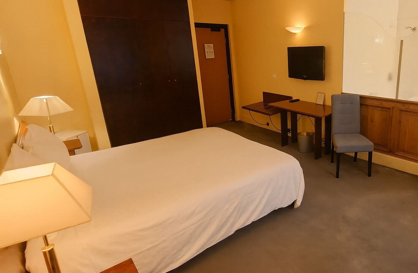 A hotel room with a bed, a desk, a chair, a TV, and a lamp.
