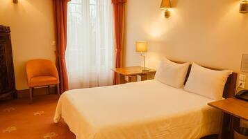 Una habitación de hotel con una cama grande, una silla, una mesita de noche y una lámpara.