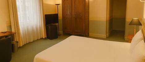 Una habitación de hotel con cama, armario, escritorio con lámpara y cubo de basura.