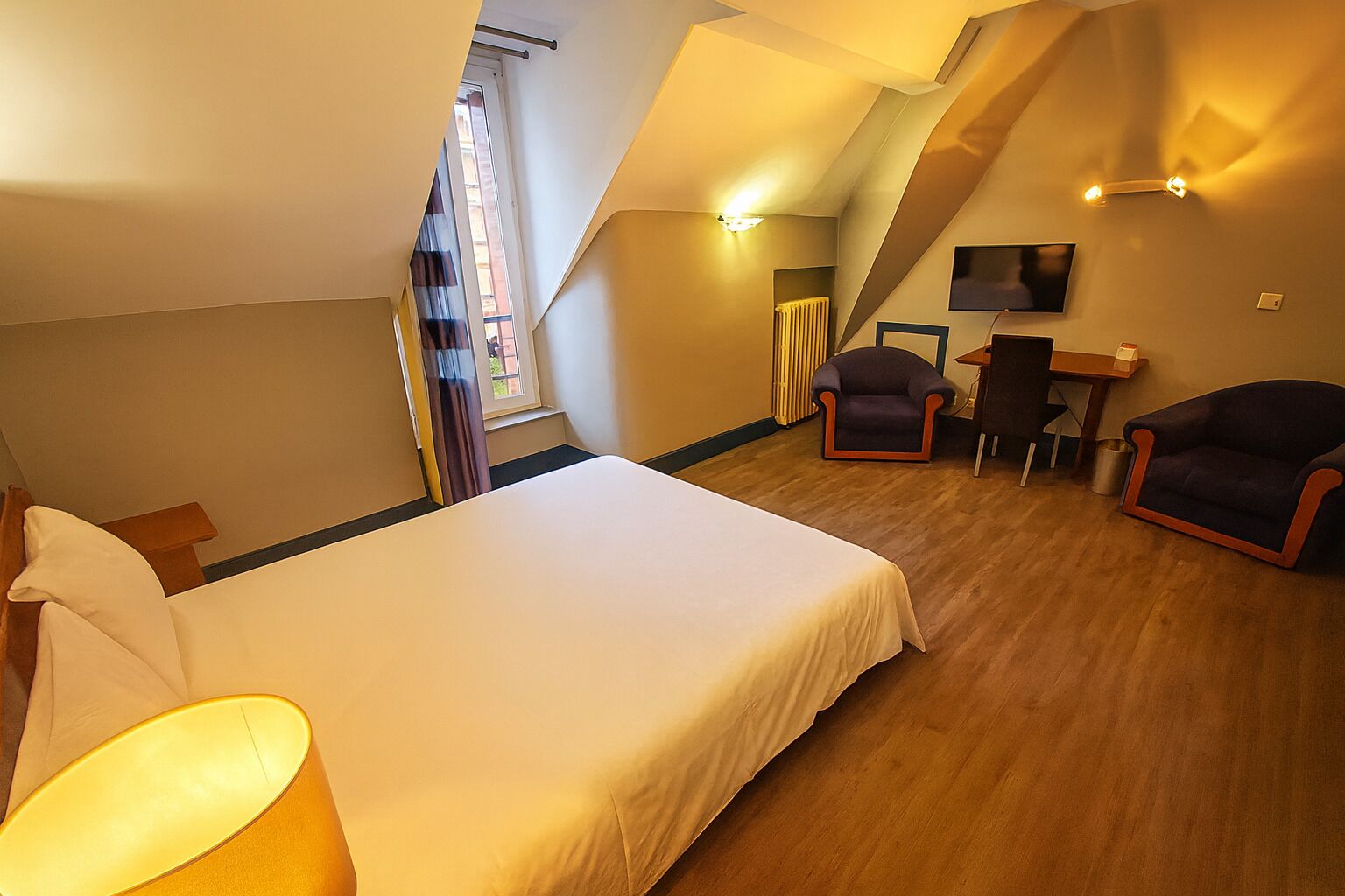 A bedroom with a bed, two armchairs, a desk, and a TV.