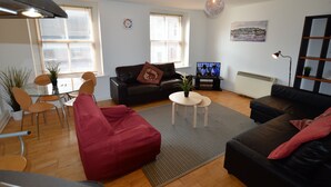 A modern living room with a black leather sofa, a red armchair, a glass dining table with chairs, and a small white coffee table. - MetroStays - Stephen's Green 7-1 (Dublin)