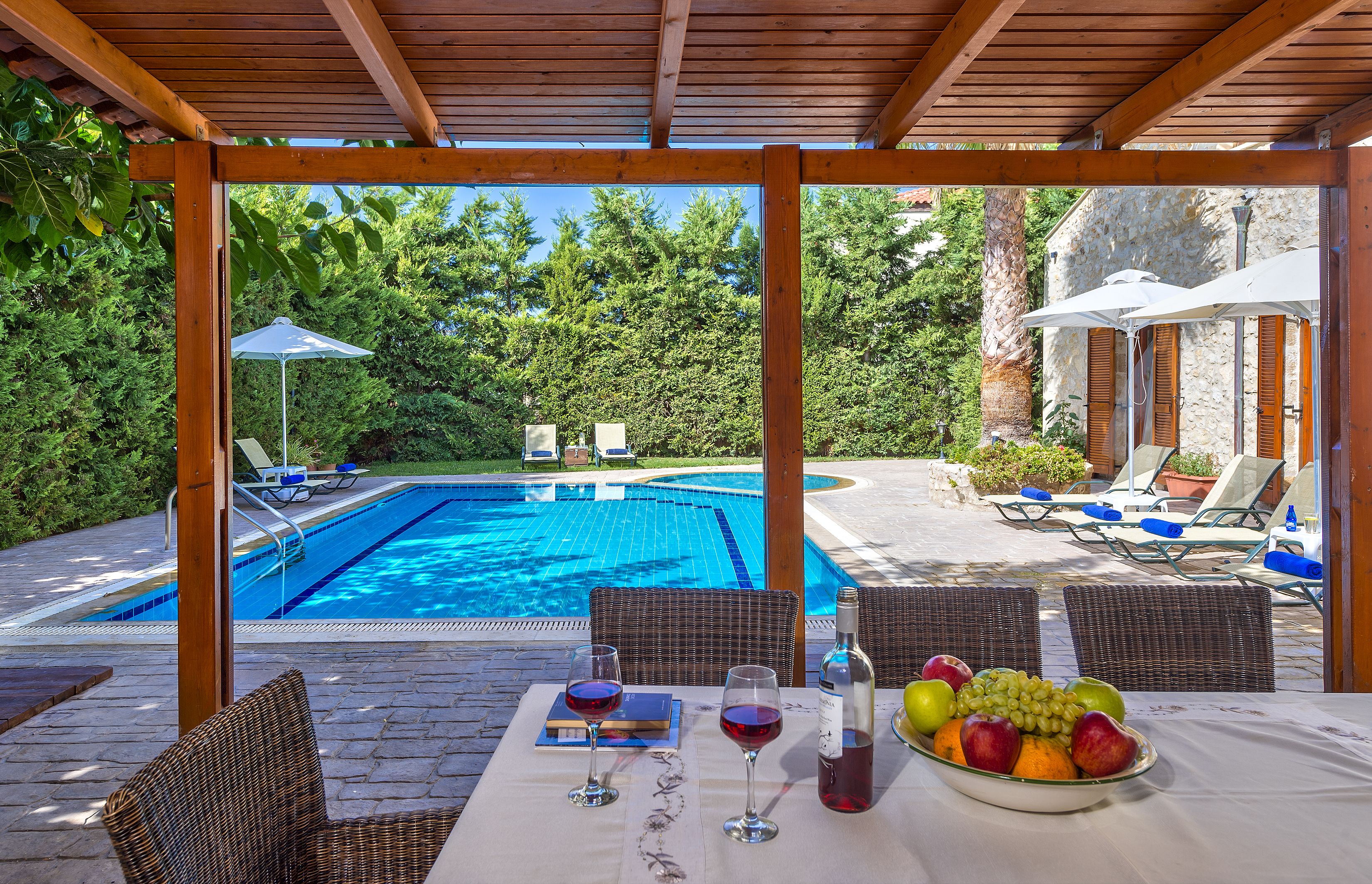 A poolside area with a table set for two, two chairs, and a view of a swimming pool.