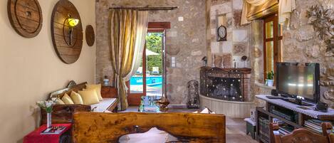 A cozy living room with a wooden sofa, a TV, and a stone wall.