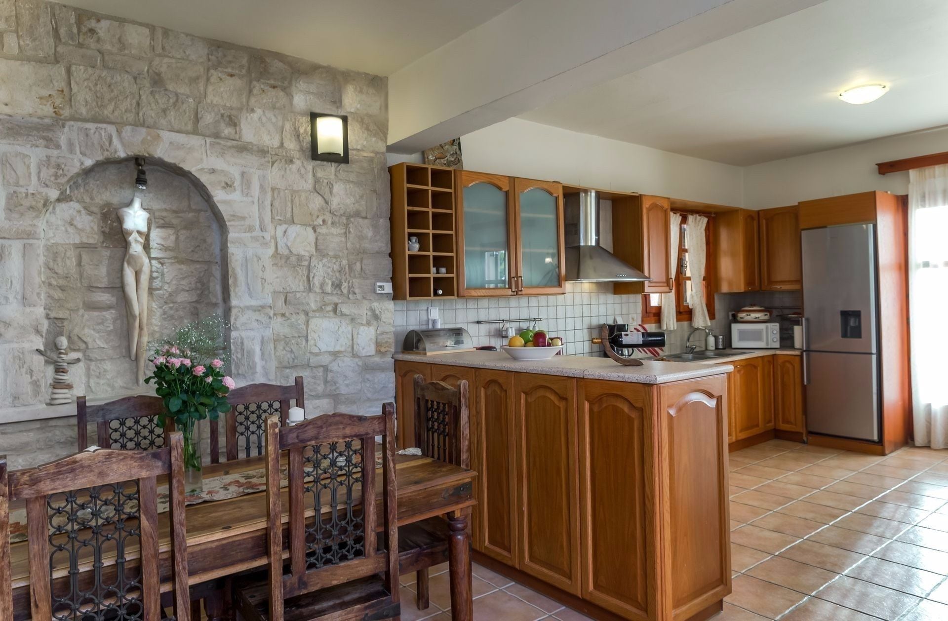 A kitchen with stone walls, wooden cabinets, a central island, and a dining area with a table and chairs.