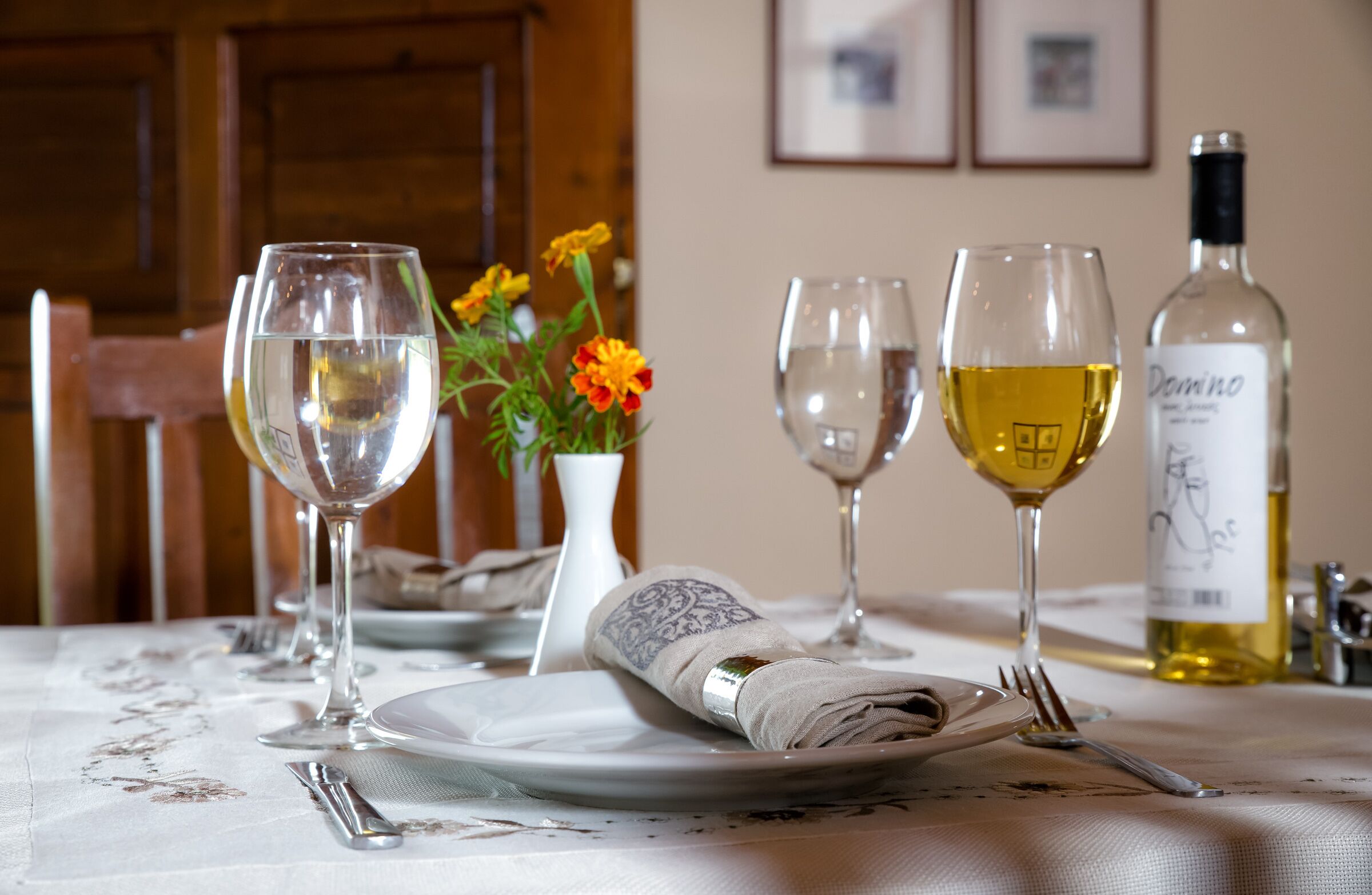 A dining table set with wine glasses, a bottle of wine, a vase with flowers, and neatly folded napkins.