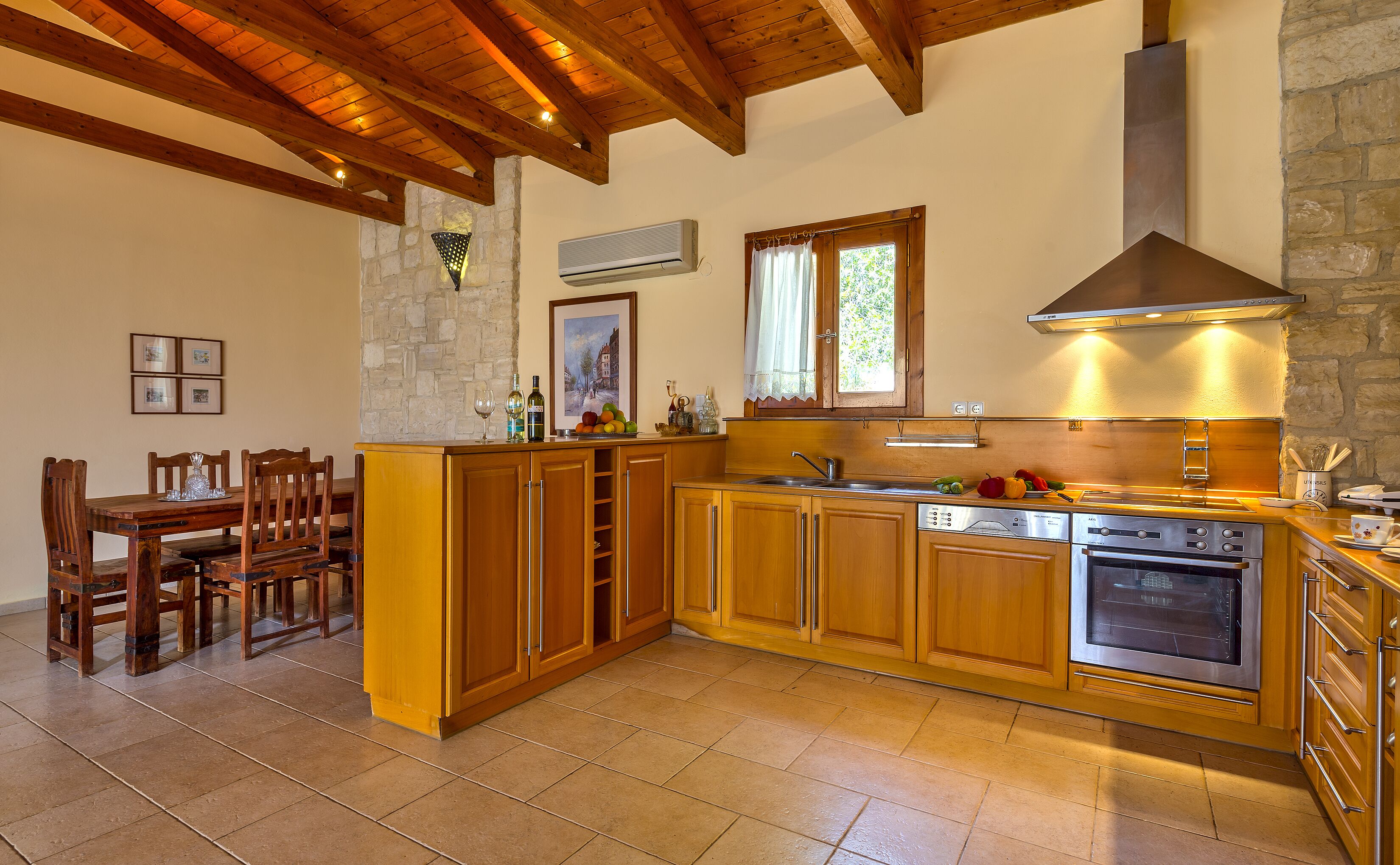 A kitchen with wooden cabinets, a stone wall, and a dining area with wooden chairs.