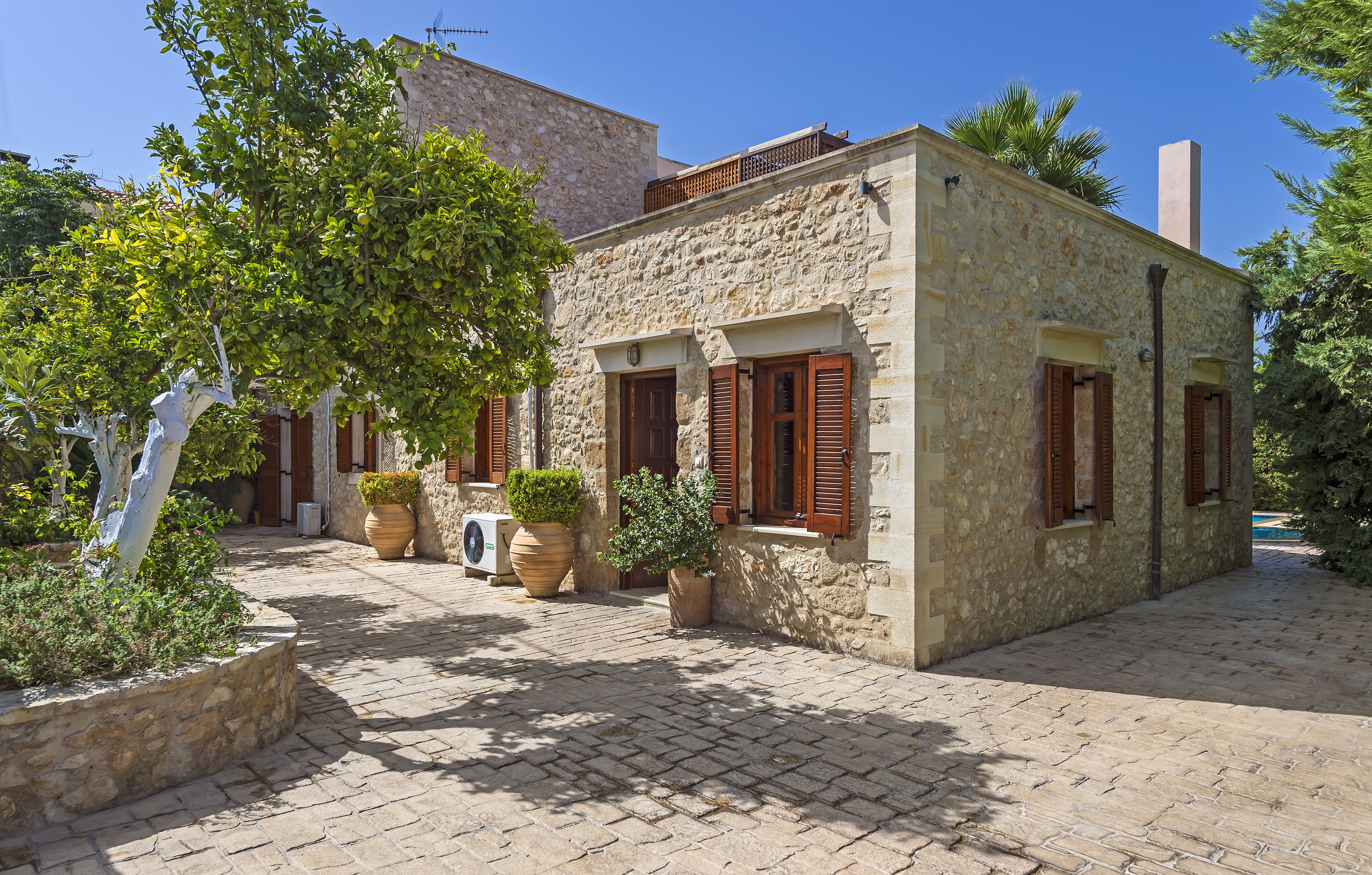 A stone building with wooden shutters, a paved courtyard, and potted plants.