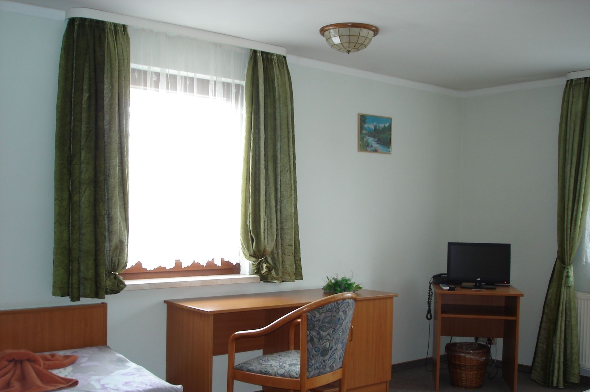 A room with a bed, a desk with a chair, a television, and a window with curtains.