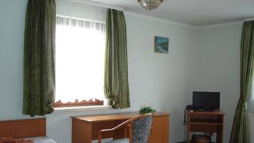 A room with a bed, a desk with a chair, a television, and a window with curtains.