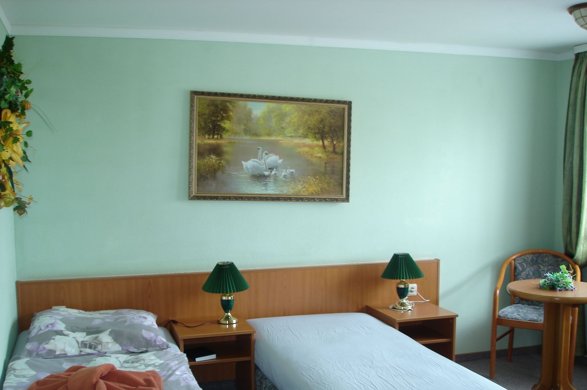 Ein Hotelzimmer mit einem Bett, zwei Nachttischen mit Lampen, einem Sessel und einem Schwane-Gemälde an der Wand.