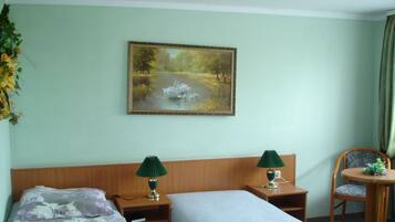 Ein Hotelzimmer mit einem Bett, zwei Nachttischen mit Lampen, einem Sessel und einem Schwane-Gemälde an der Wand.