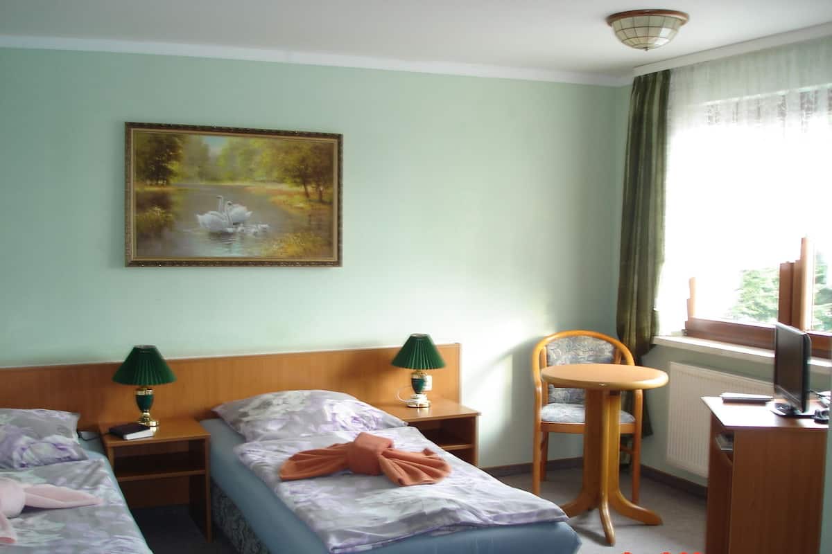 Een hotelkamer met twee bedden, een bureau, een stoel, een schilderij en een raam met gordijnen.