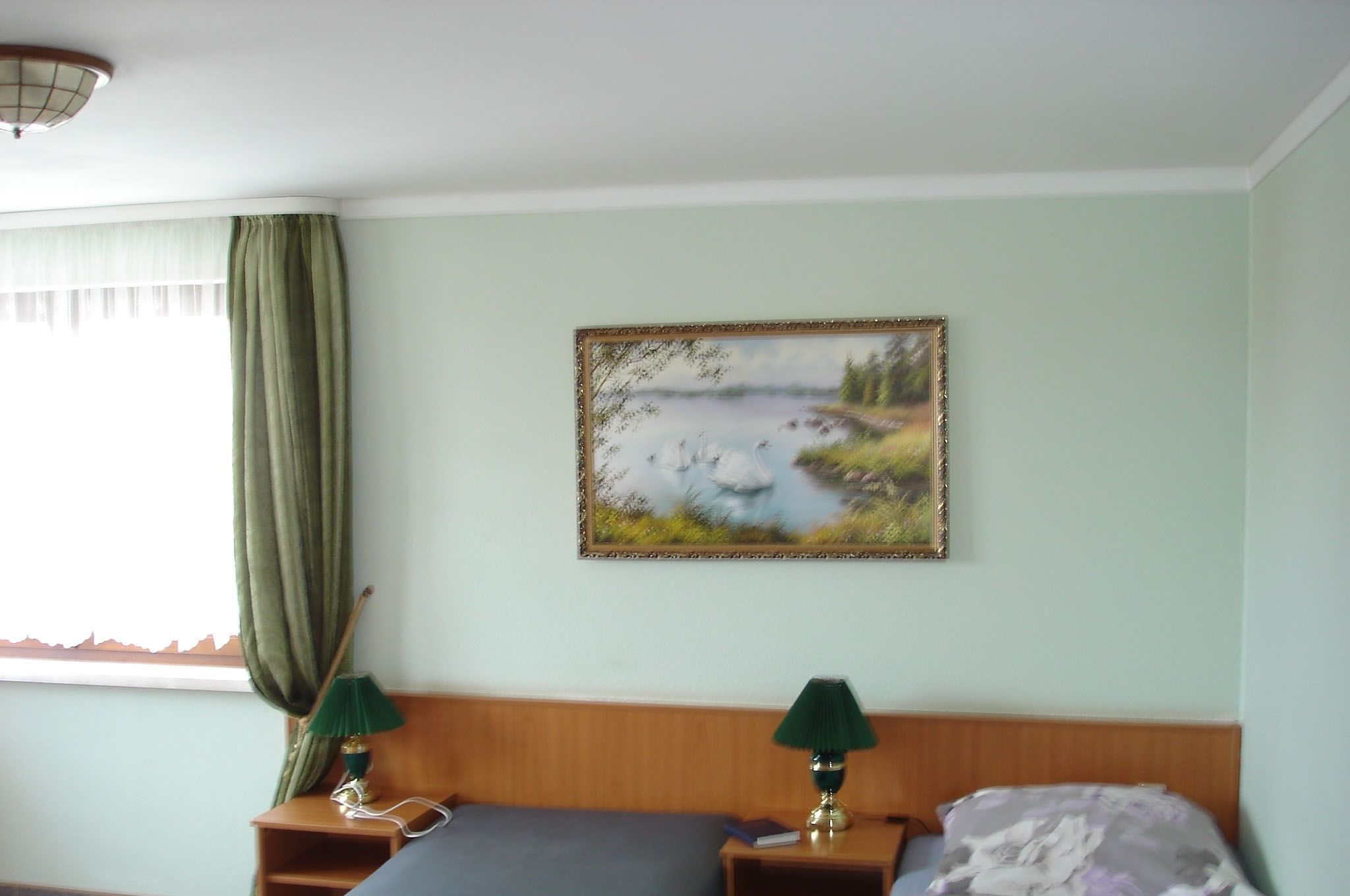 Ein Schlafzimmer mit einem Bett, zwei Nachttischen mit Lampen, einem Landschaftsbild und einem Fenster mit Vorhängen.