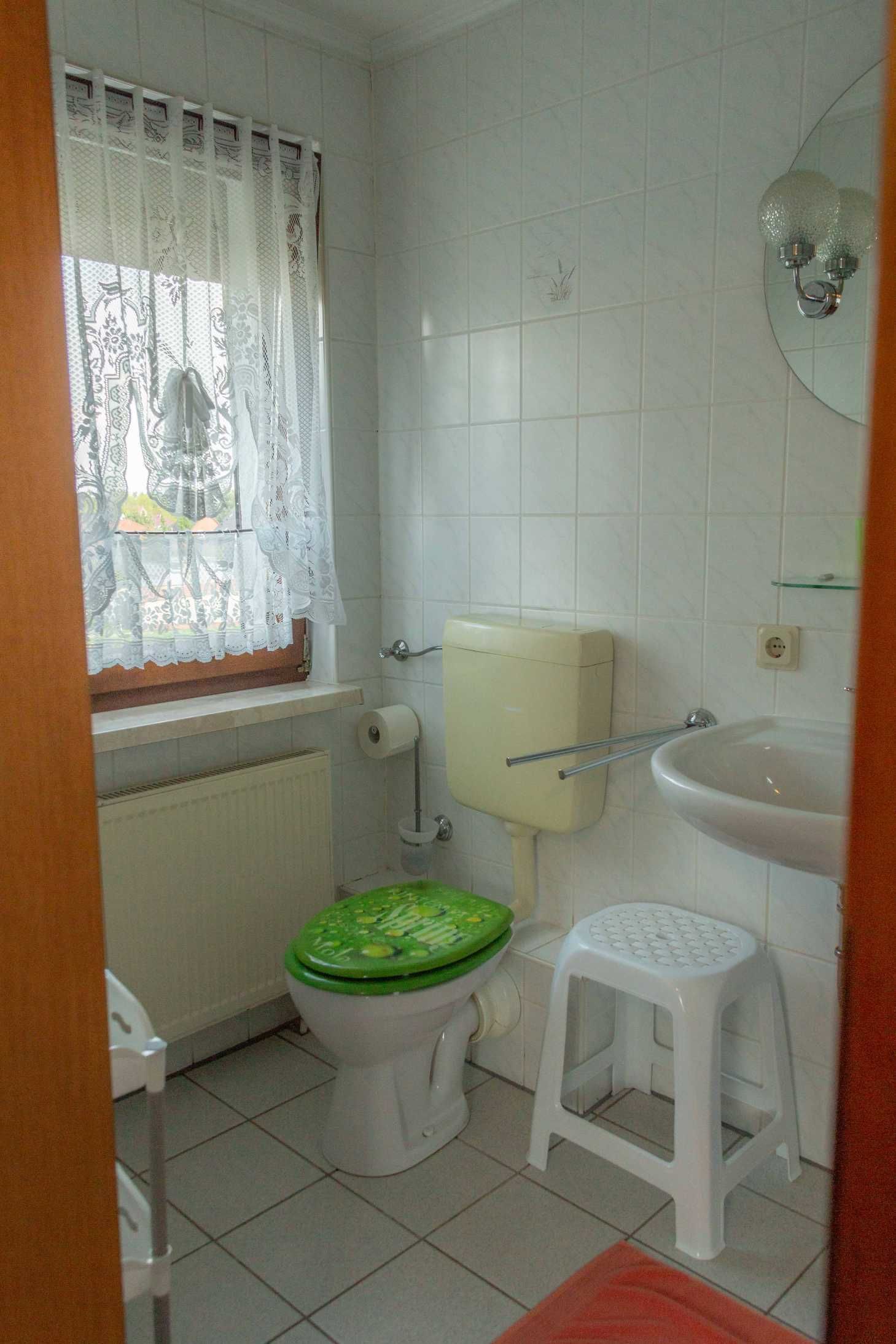 A small bathroom with a toilet, a sink, and a window with a curtain.