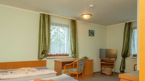 Een kamer met twee bedden, een bureau, een stoel, een televisie en een raam met gordijnen.