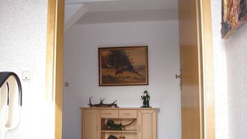 Un corridoio con un armadietto in legno, un quadro raffigurante una scena di bosco e una porta che conduce in un'altra stanza.