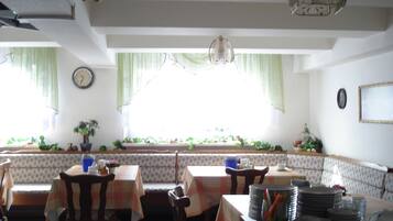 A dining area with tables and chairs, a clock on the wall, and a window with curtains.