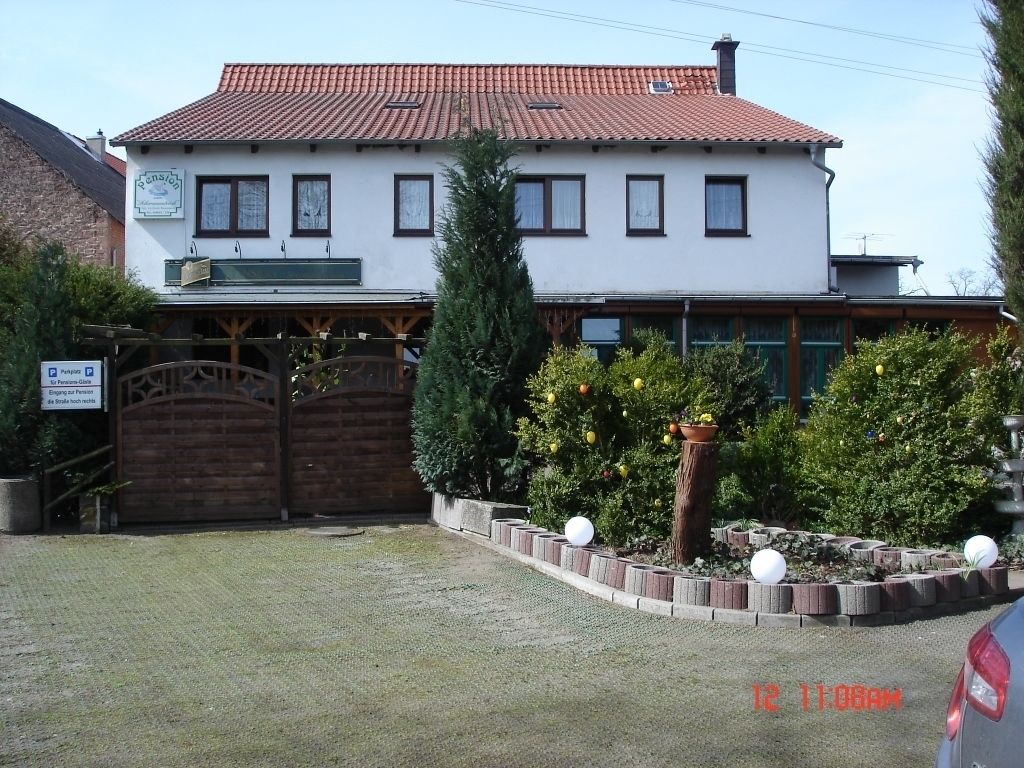 A two-story building with a red-tiled roof, a wooden fence, and a sign indicating a parking area.