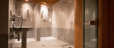 Un baño moderno con lavamanos independiente, múltiples cabezales de ducha y zona de ducha con mampara de vidrio.