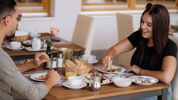 A dining table with plates of food, cups, and a basket of bread.